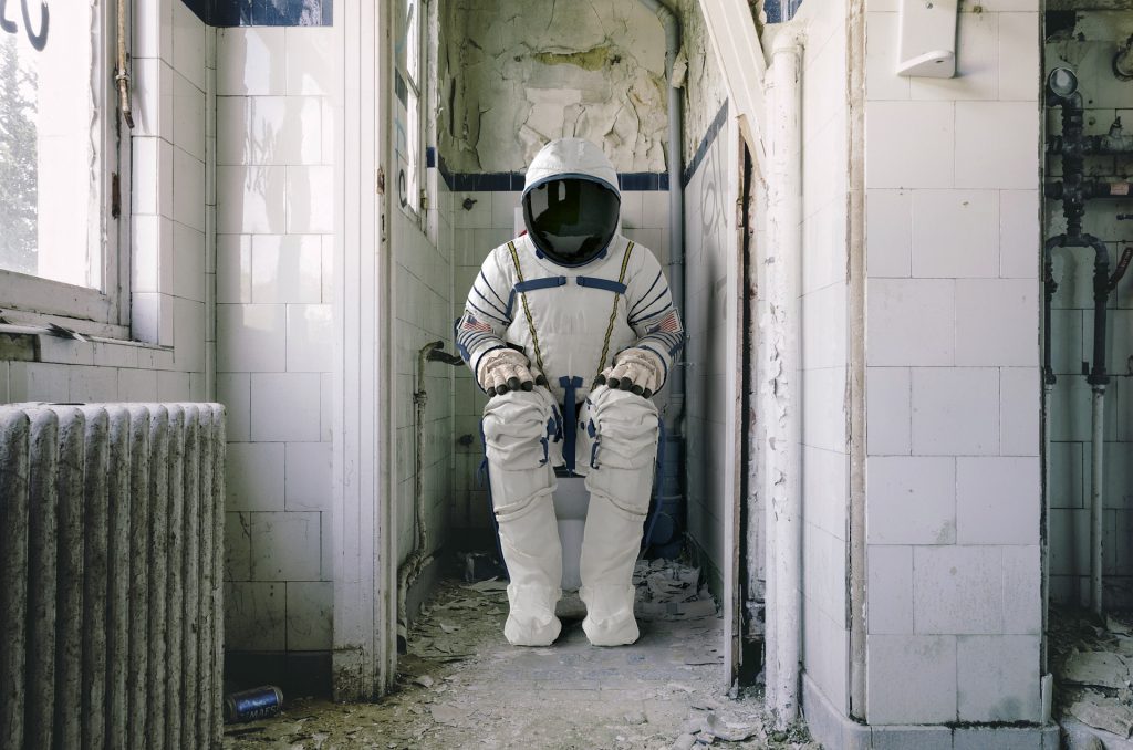 Astronaut sitting on a toilet.